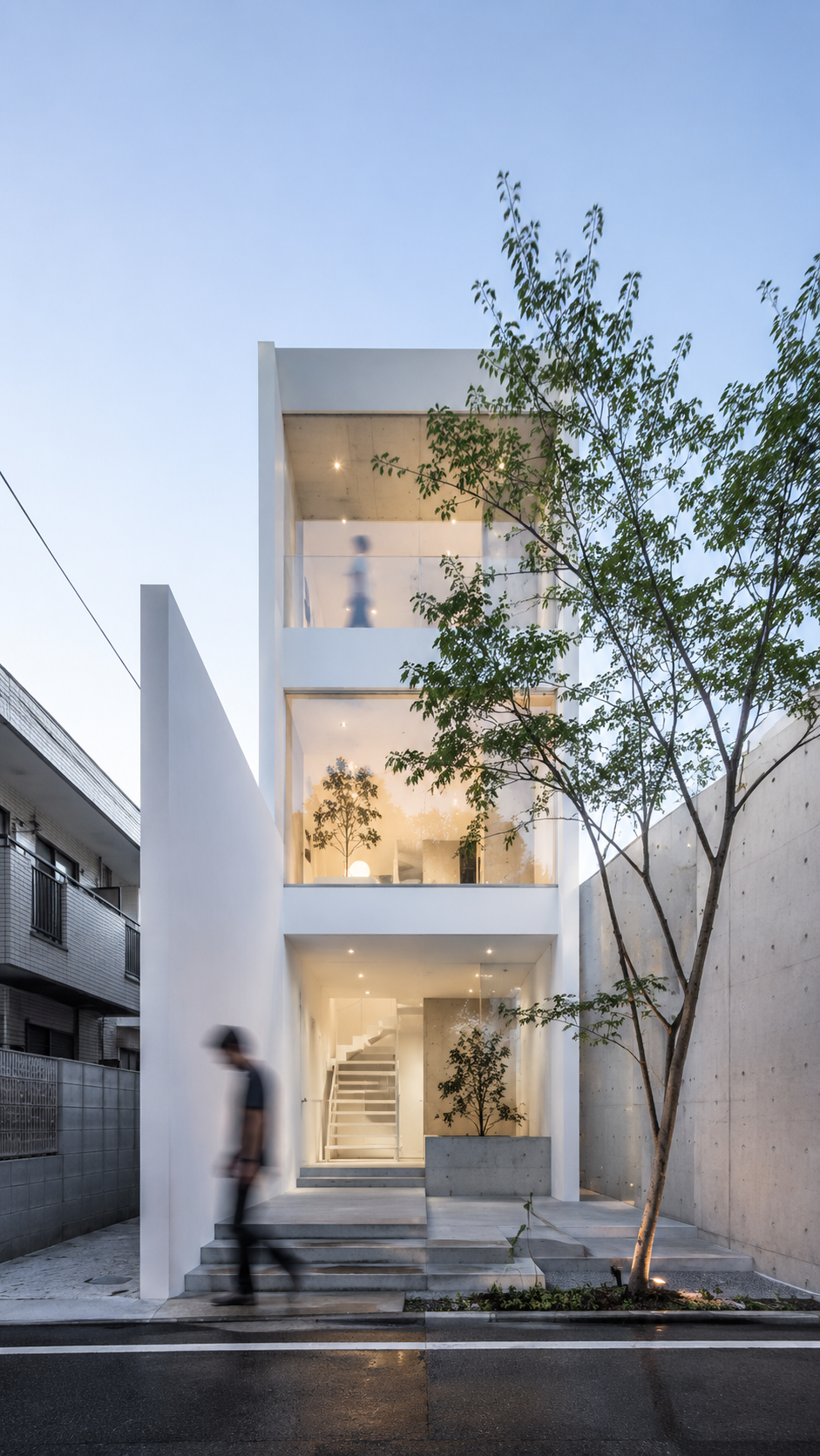 Edificio angosto de tres niveles con árbol al frente